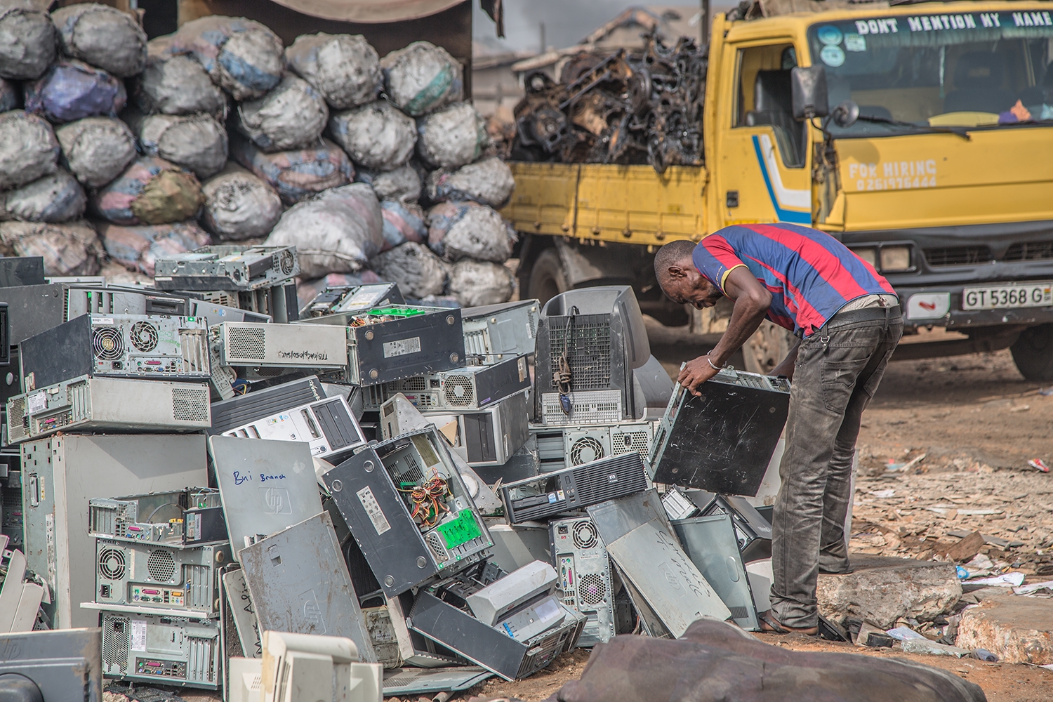 Image du documentaire "welcome to sodom" montrant un africain penché sur un tas d'ordinateurs fixes en vrac sur un sol de terre en plein air